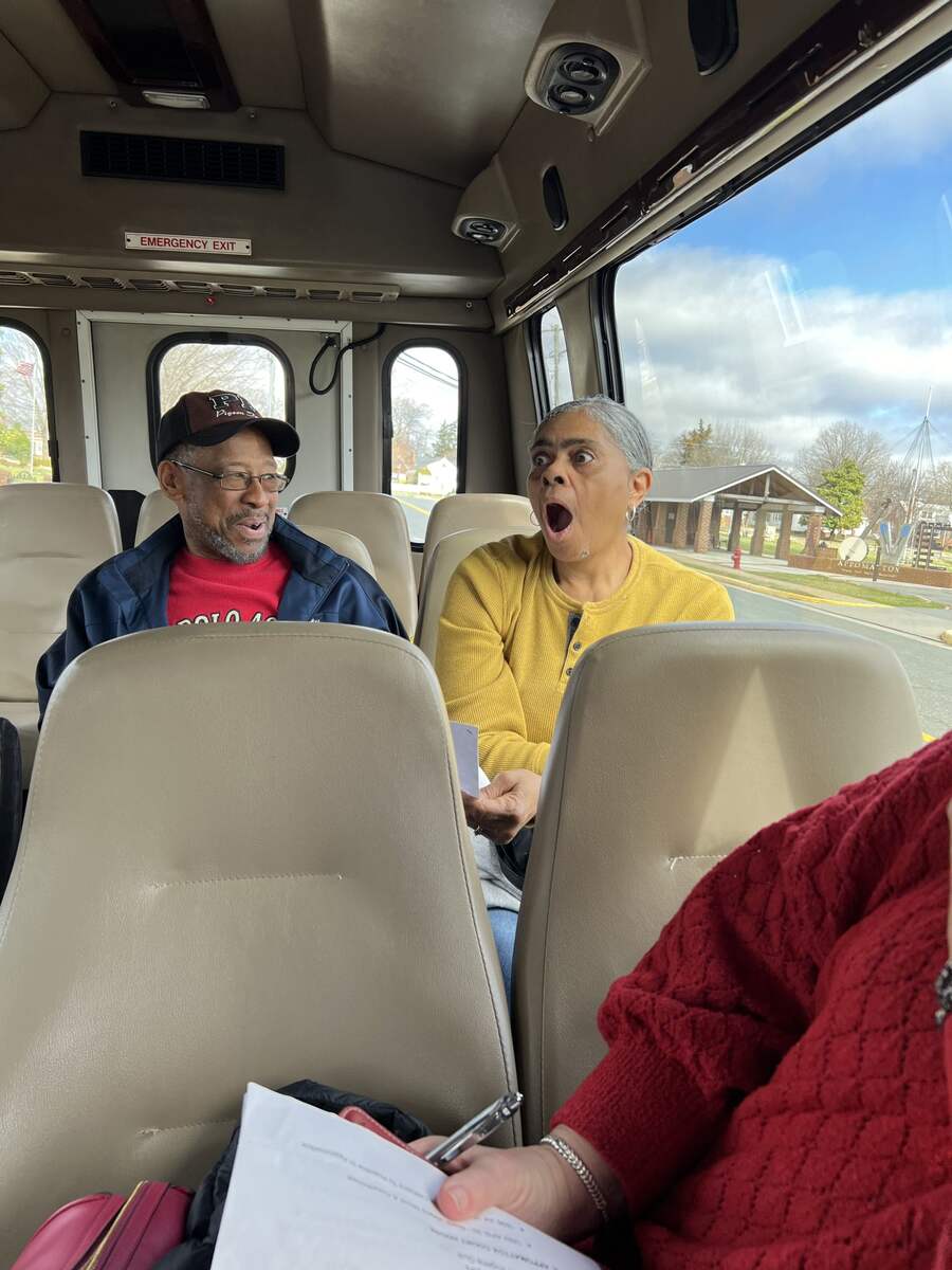 Man and woman sitting on tour bus, woman has mouth open